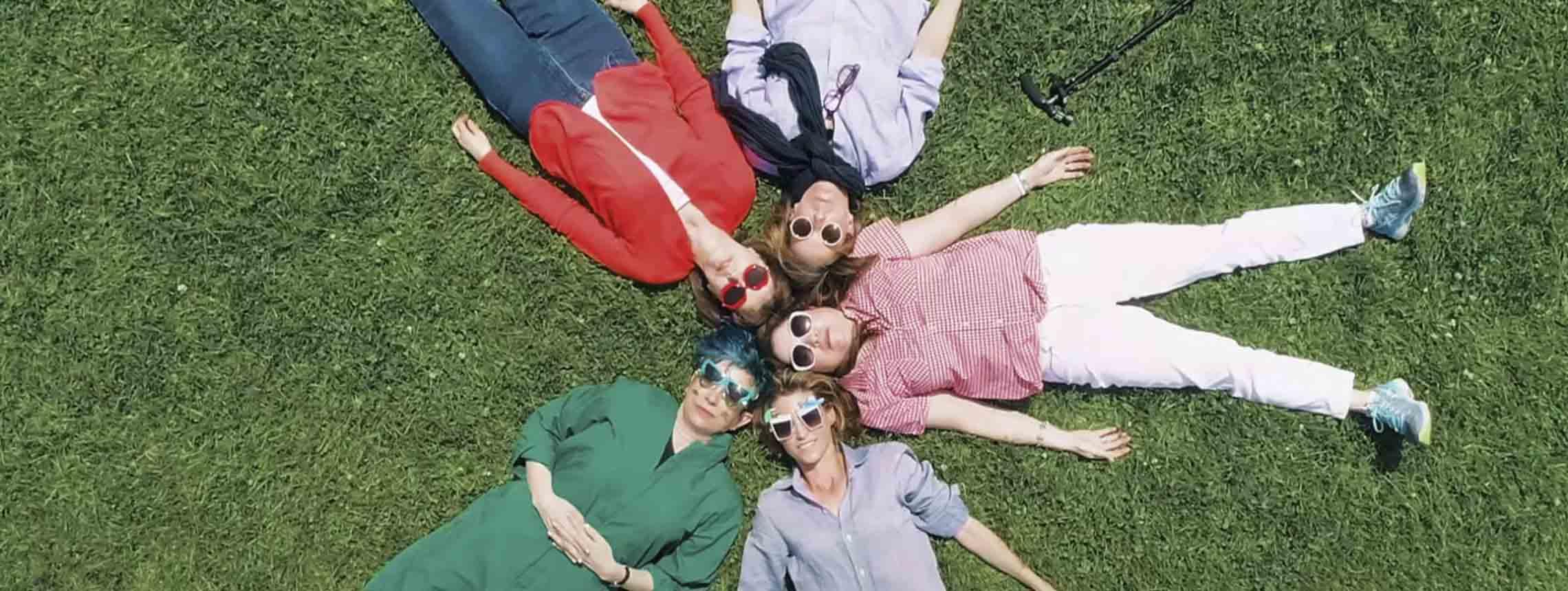 Familie liegt im Kreis auf dem Rasen und schaut mit Sonnenbrillen in den Himmel