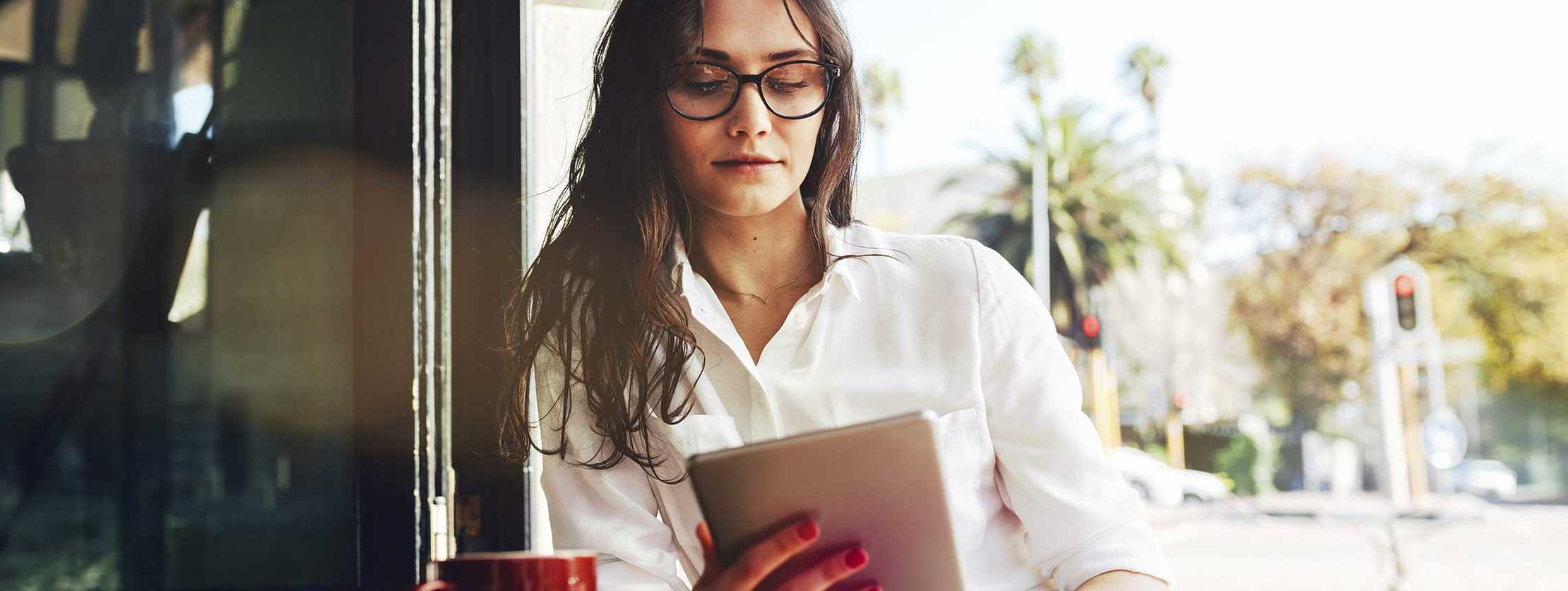 Junge Frau liest etwas auf ihrem Tablet in einem Café