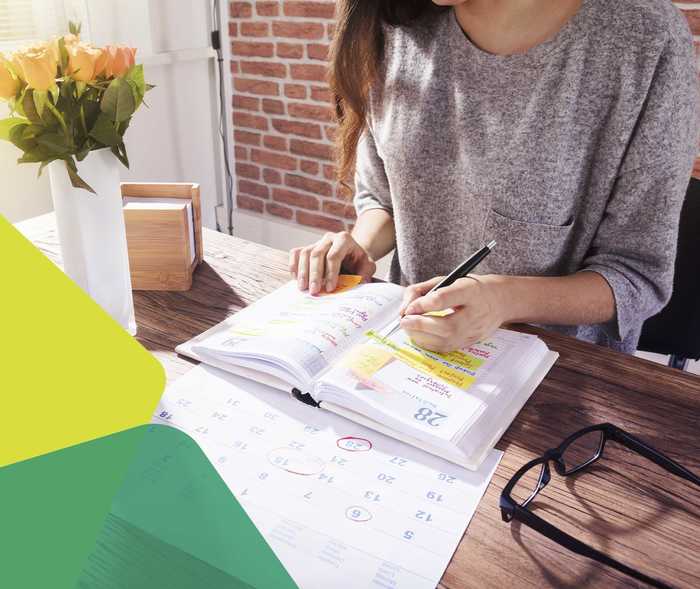 Das Bild zeigt eine Frau, die etwas in ihren Kalender einträgt