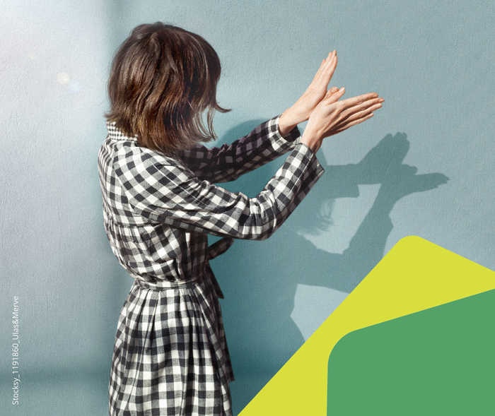 Eine Frau wirft mit ihren Händen ein Schattenbild an die Wand hinter ihr.