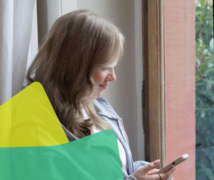 Kerstin steht vor einem Fenster und hält ein Smartphone in ihrer Hand.