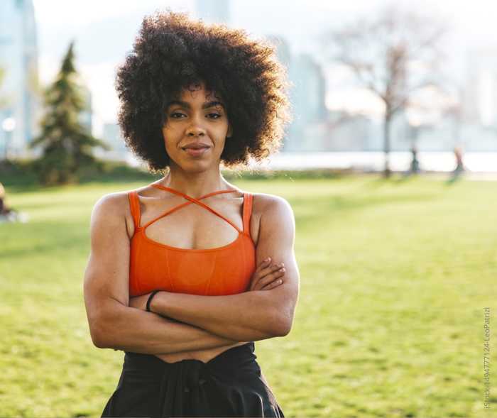 Eine junge Frau steht mit verschränkten Armen und schaut in die Kamera.