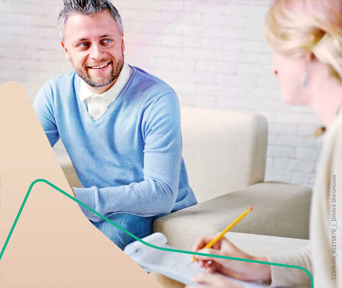 Ein Mann sitzt auf einem Sofa und wird von einer Frau interviewt.