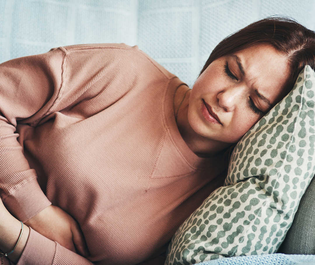 Das Bild zeigt eine Frau die auf der Seite liegt und die Arme vor dem Bauch verschränkt