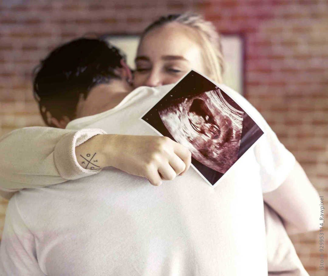 MS und ich: Eine glückliche Frau umarmt ihren Partner. In der Hand hält sie ein Ultraschallbild 