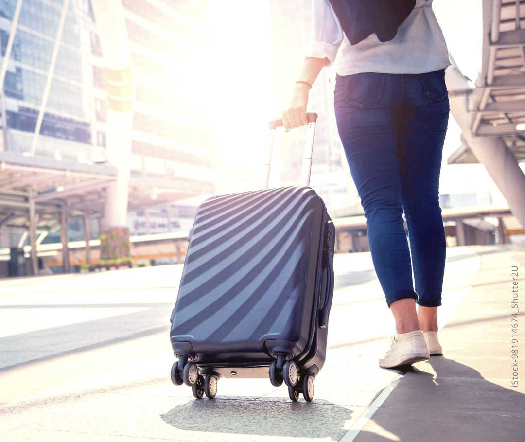 MS und ich: Eine Frau zeiht bei strahlendem Sonnenschein einen vierrädigen Koffer hinter sich her