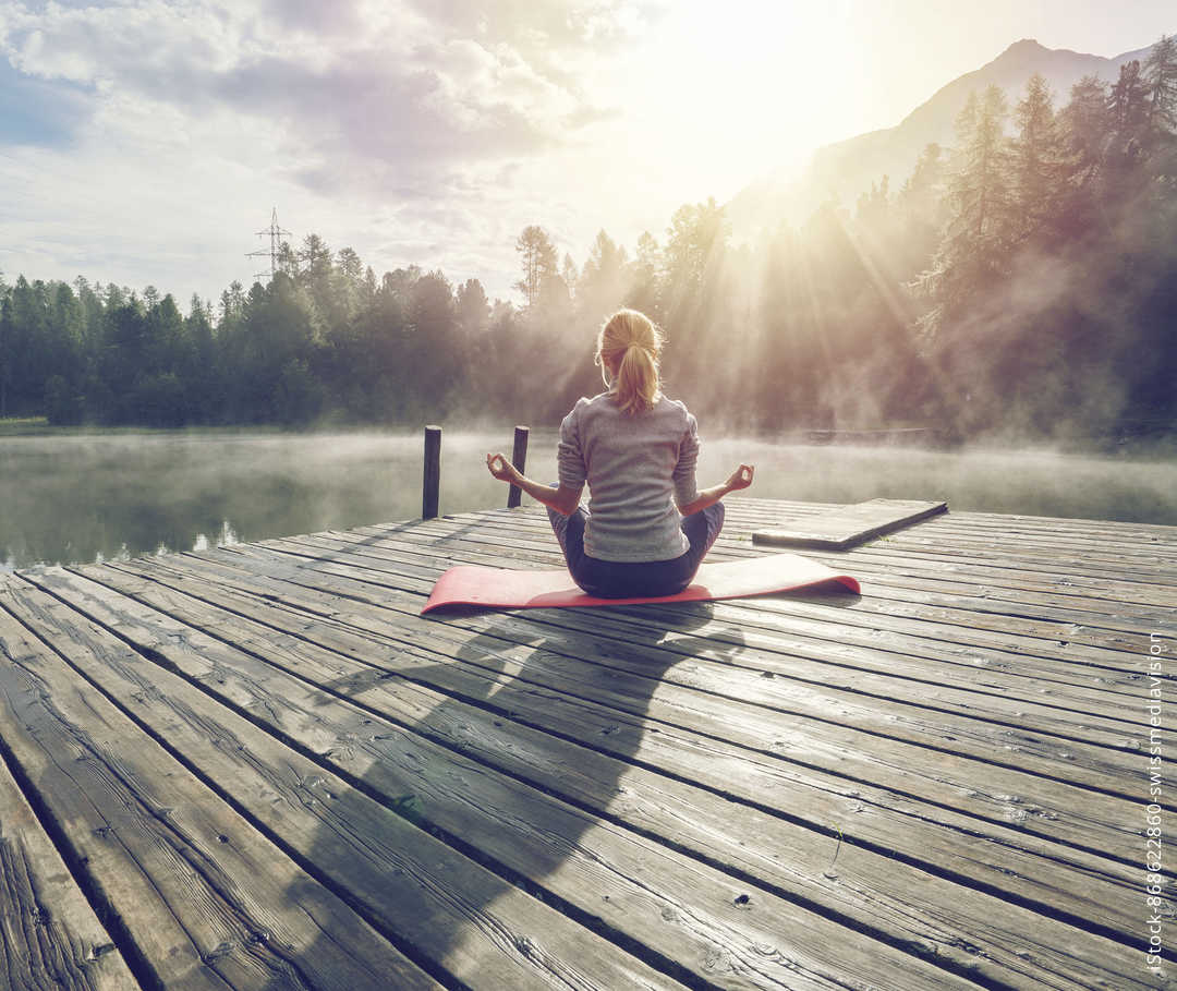Eine blonde Frau macht Yoga auf einem Steg am See
