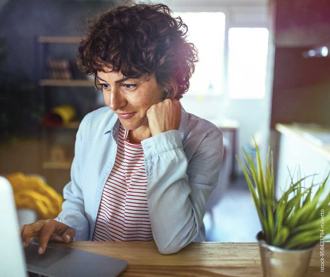 Eine Frau stützt ihren Kopf auf die Hand und informiert sich an ihrem Laptop