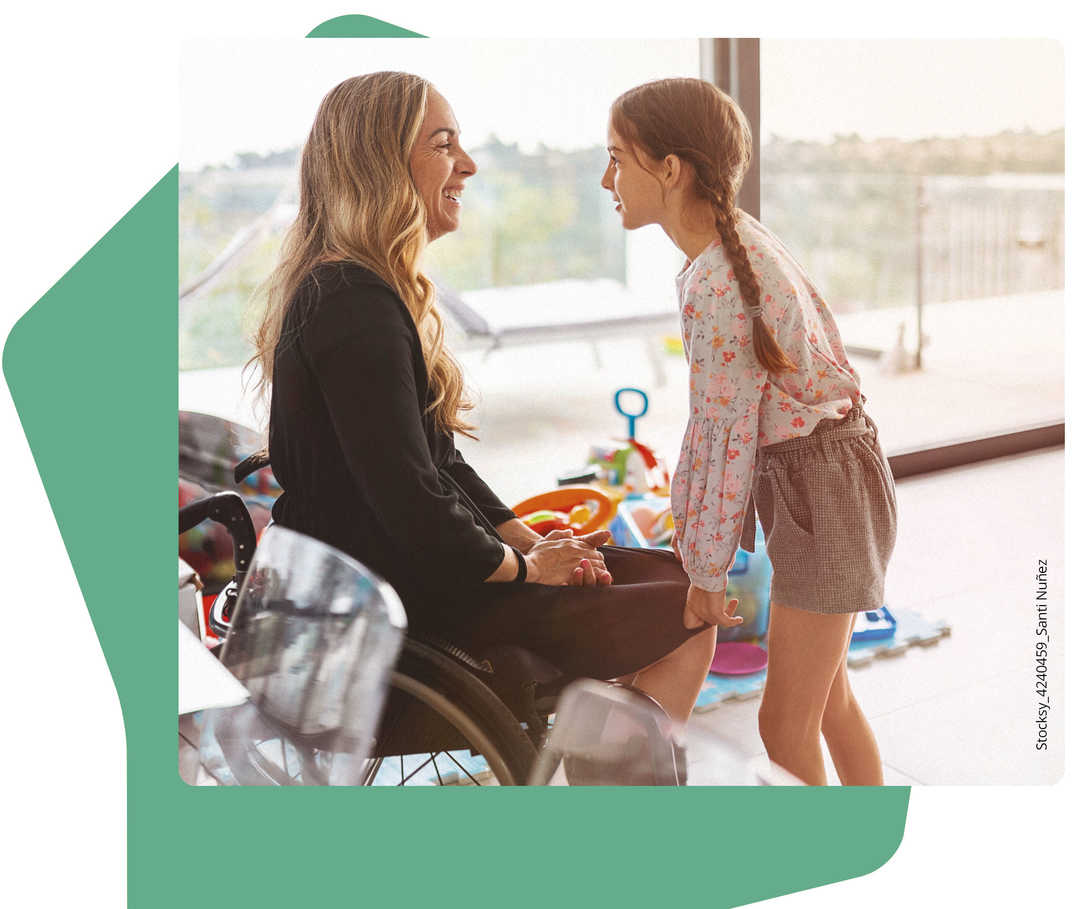 Ein kleines Mädchen stützt sich mich ihren Händen auf die Knie ihrer Mutter, die im Rollstuhl sitzt