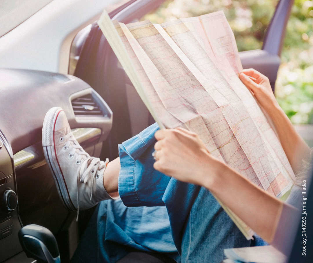 Eine aufgeschlagene Landkarte wird von einer Person im Auto angeschaut.