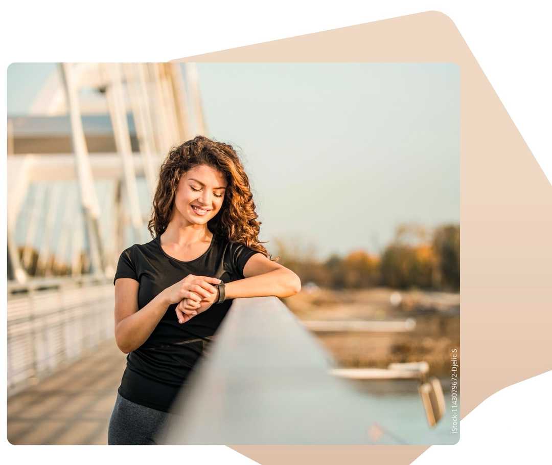 Mutiple Sklerose früh behandeln Eine junge Frau steht auf einer Brücke und schaut auf ihre Armbanduhr.