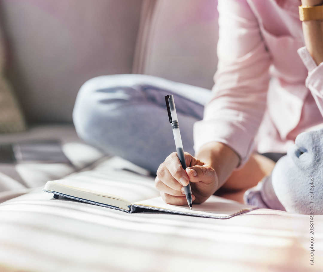 Person schreibt mit einem Stift in ein Notizbuch.