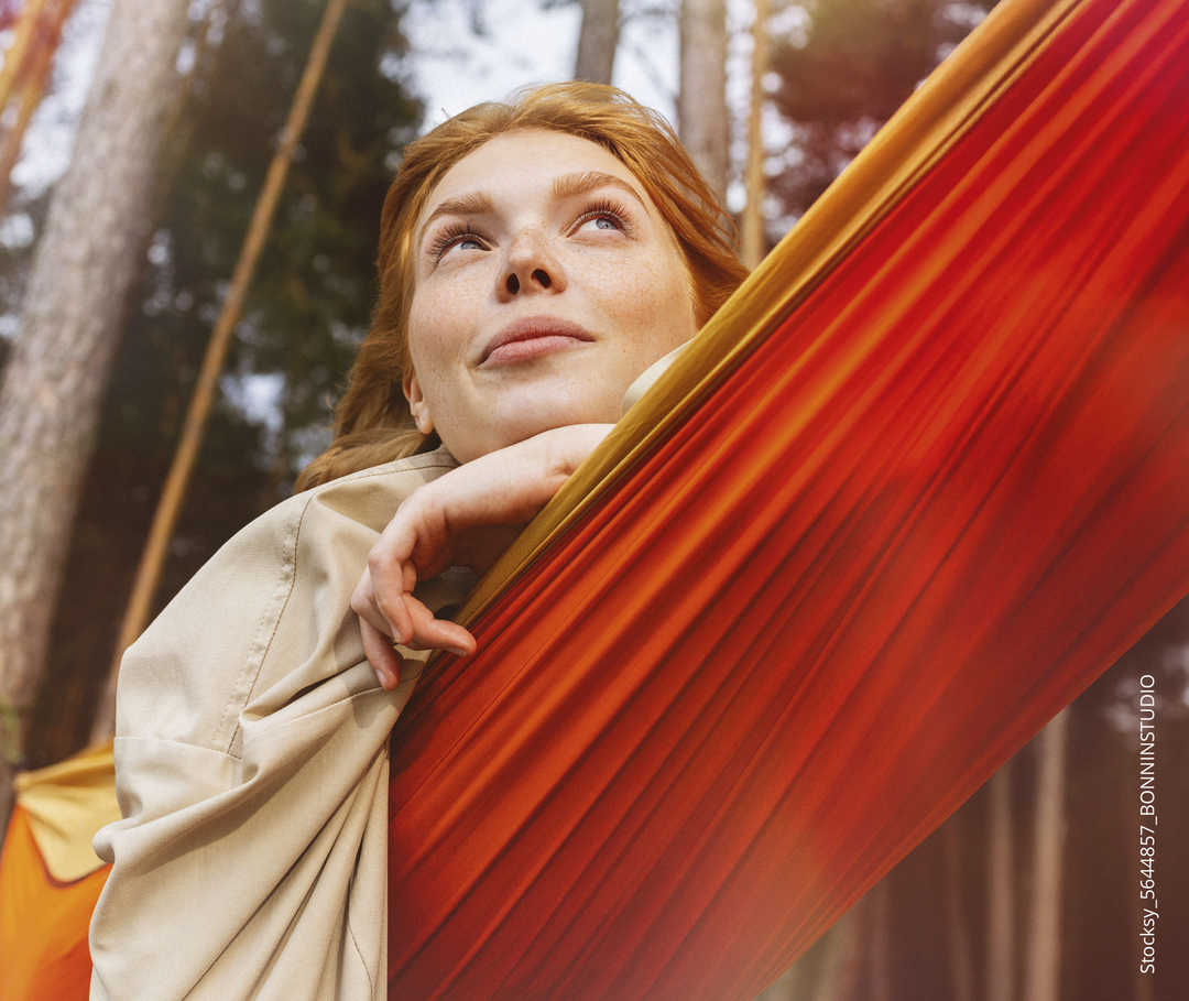 Frau liegt in Hängematte und schaut in den Himmel.